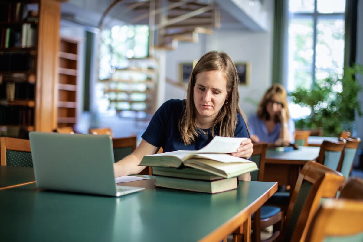 A visually impaired young woman sitting and studying in the university library. Young female using books and laptop.
